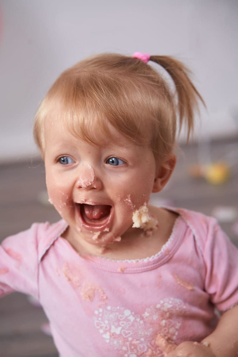 Klein meisje lacht blij met cake op gezicht tijdens cakesmash fotoshoot eerste verjaardag — Familieshoot Stefan Segers