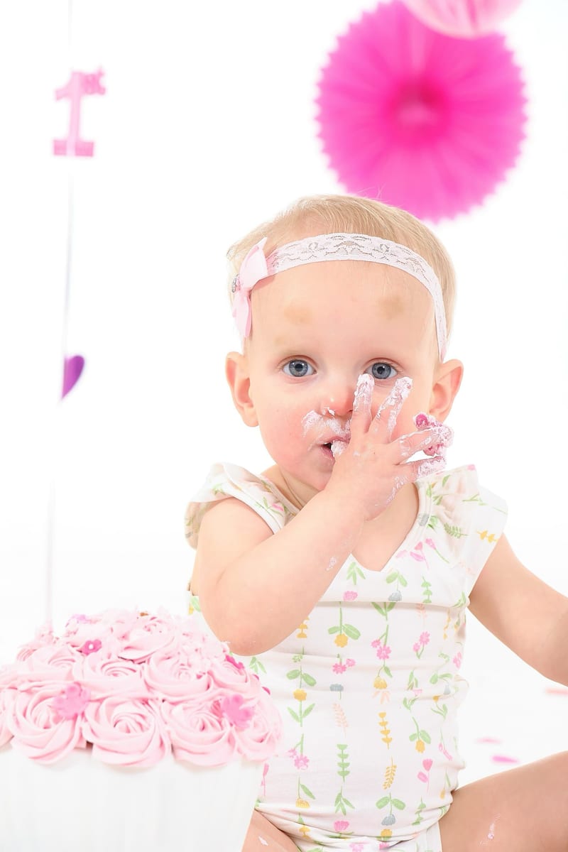 Lachend meisje eet roze verjaardagstaart, cakesmash fotoshoot eerste verjaardag, babyfotografie studio Zoetermeer — Familiesh