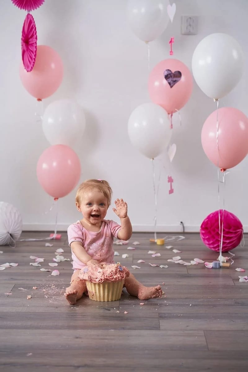 Lachend meisje op eerste verjaardag met cupcake, roze ballonnen decoratie cakesmash fotoshoot — Familieshoot Stefan Segers