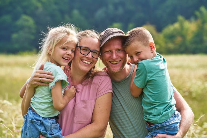 Gelukkig gezin met twee kinderen lacht buiten in groen landschap, familiefotoshoot Westerpark — Familieshoot Stefan Segers