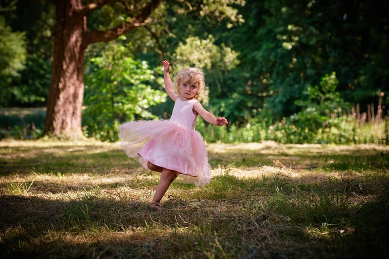 Klein meisje in roze jurkje speelt vrolijk in het bos, familiefotografie Westerpark Zoetermeer — Familieshoot Stefan Segers