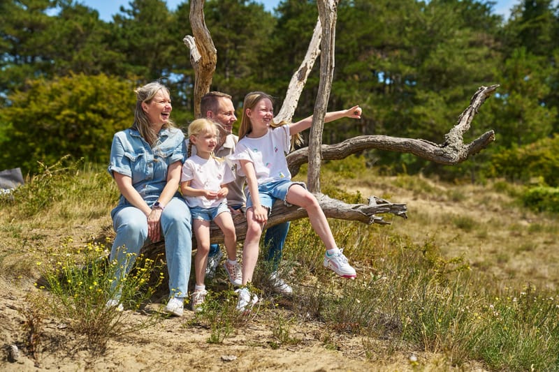 Gezin zit samen op dode boom in natuur, lachende ouders en kinderen buiten familiefotografie Zoetermeer — Familieshoot Stefan