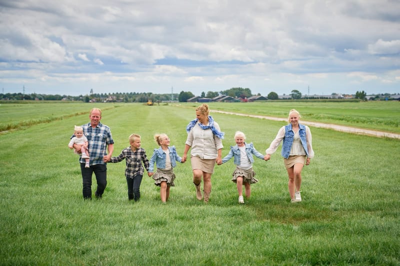Groot gezin loopt hand in hand door groen weiland, blije familiefotoshoot Zoetermeer platteland — Familieshoot Stefan Segers