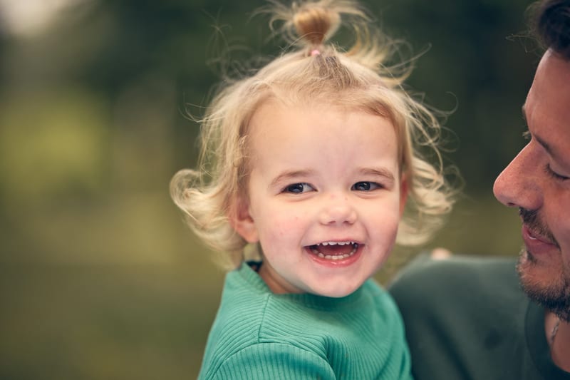 Blond meisje lacht naar vader buiten, warme familiefotoshoot Zoetermeer — Familieshoot Stefan Segers