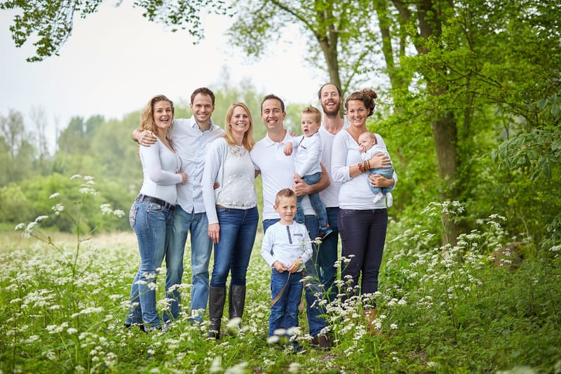 Grote uitgebreide familie met kinderen staat lachend in groen veld, professionele familiefotoshoot Zoetermeer — Familieshoot