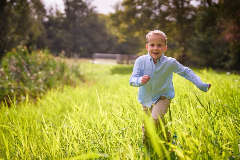 Blij jongetje rent lachend door groen veld, kinderfotografie buiten Zoetermeer — Familieshoot Stefan Segers
