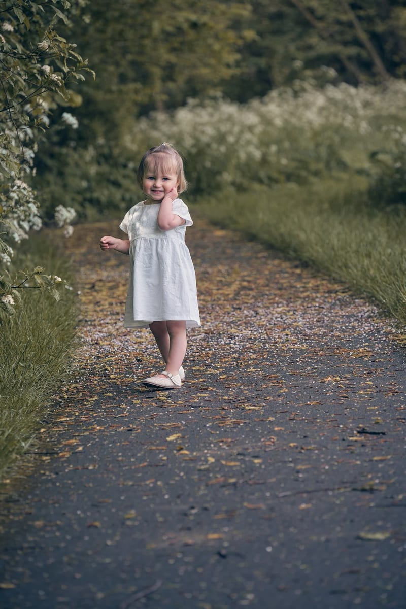 Peuter meisje loopt lachend op tuinpad tussen bloeiende struiken, kinderfotografie Zoetermeer — Familieshoot Stefan Segers