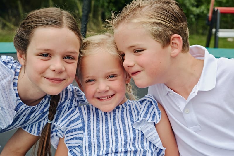 Drie kinderen lachen samen in de tuin, vrolijke kinderfotoshoot Zoetermeer — Familieshoot Stefan Segers