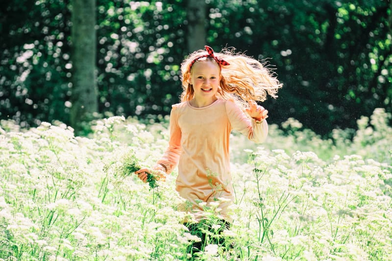 Gelukkig meisje rent lachend door wit bloemenvel in natuur, kinderfotografie Zoetermeer — Familieshoot Stefan Segers
