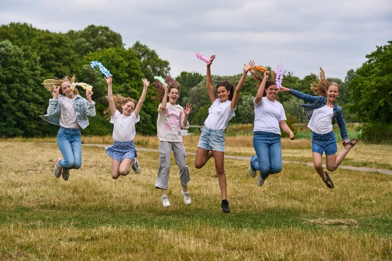 Groep kinderen springt blij in de lucht op weiland, kleurrijk kinderfeestje fotoshoot Zoetermeer — Familieshoot Stefan Segers