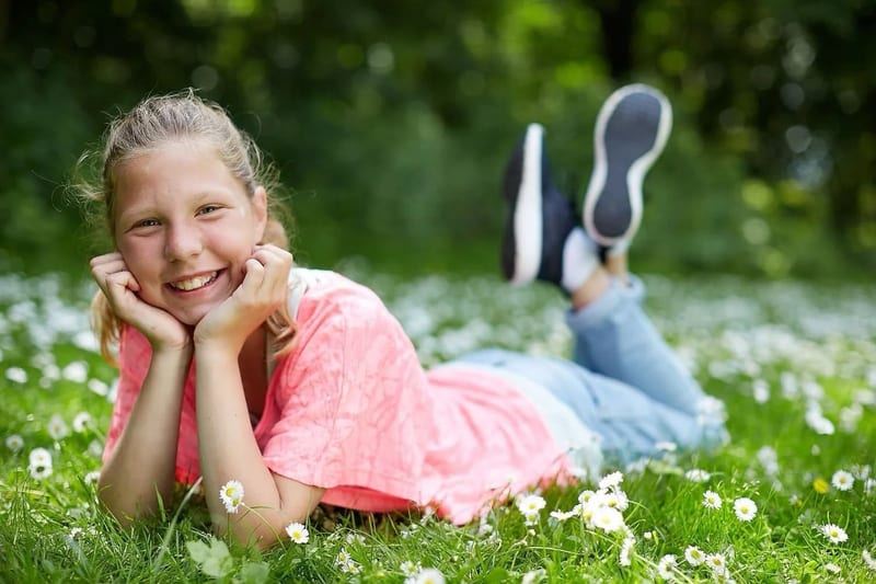 Blij meisje ligt lachend in gras met witte bloemen, kinderfotoshoot verjaardag Zoetermeer — Familieshoot Stefan Segers