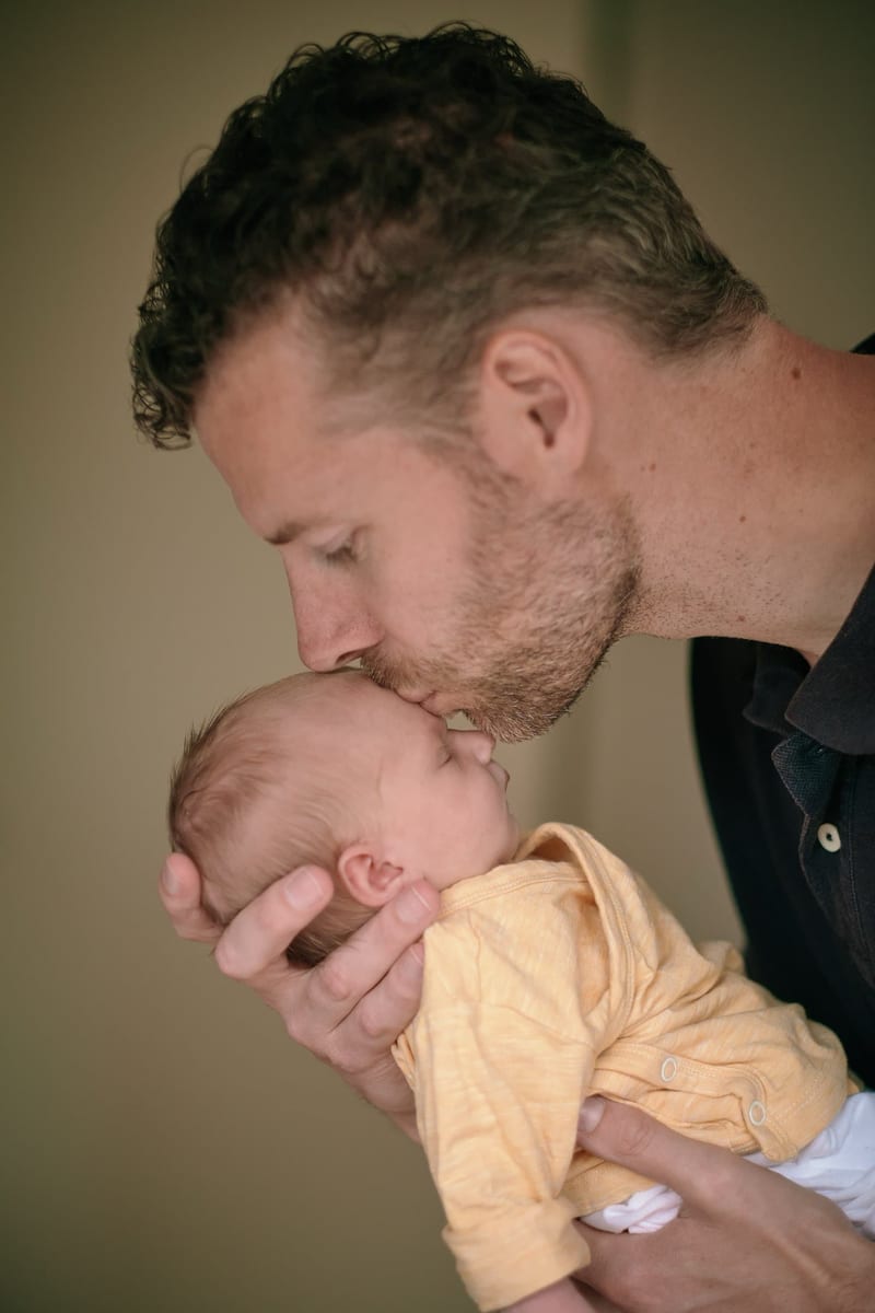 Vader kust pasgeboren baby in geel shirtje, tedere newbornfotoshoot Zoetermeer — Familieshoot Stefan Segers