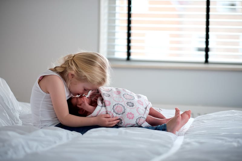 Blond meisje knuffelt pasgeboren baby op wit bed, tendre newborn fotoshoot Zoetermeer — Familieshoot Stefan Segers