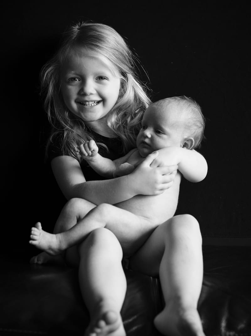 Groot meisje knuffelt lachend pasgeboren baby, newbornfotoshoot zwart-wit fotostudio Zoetermeer — Familieshoot Stefan Segers