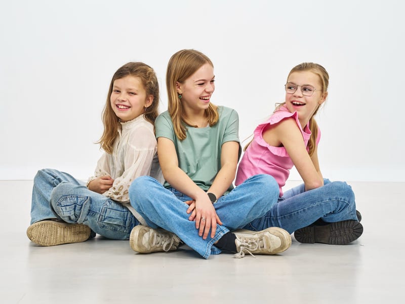 Drie gelukkige meisjes zitten samen in fotostudio, lachend en ontspannen, studiofotografie familieshoot — Familieshoot Stefan