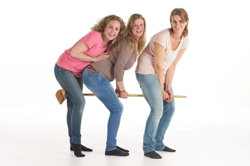 Drie vriendinnen lachen samen op houten bank, speelse vrijgezellenfeest fotoshoot Zoetermeer — Familieshoot Stefan Segers