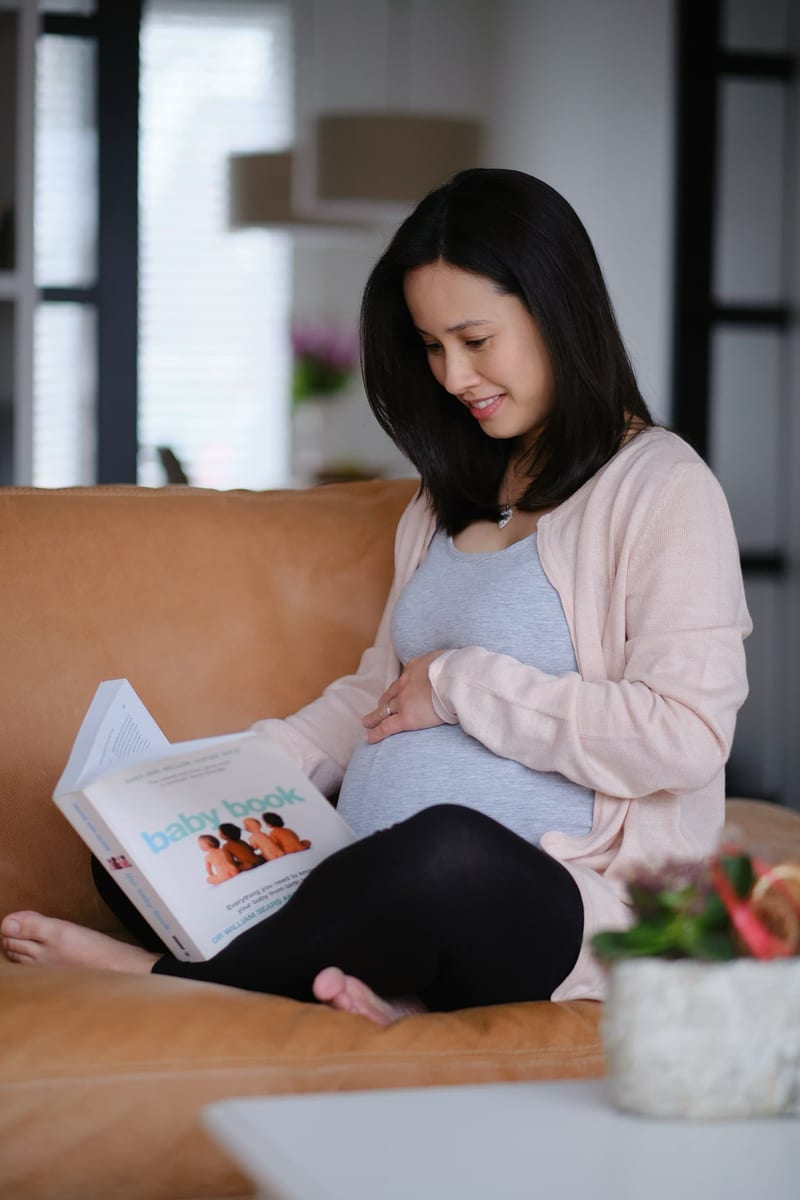 Zwangere vrouw zit op bank met fotoboek, glimlacht naar buik, maternity fotoshoot Zoetermeer — Familieshoot Stefan Segers