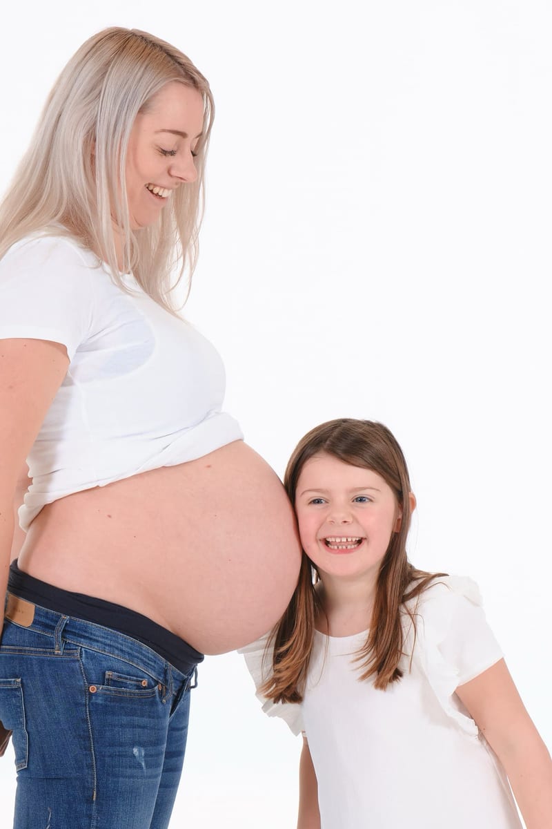 Zwangere moeder en dochter lachen samen in studio, maternity shoot fotografie Zoetermeer — Familieshoot Stefan Segers