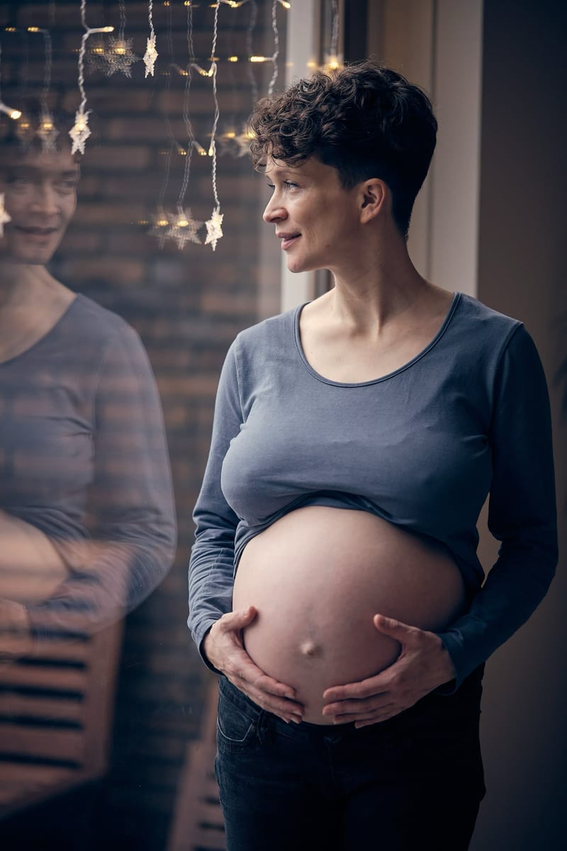 Zwangere vrouw met buik in warm licht en slingers, intieme zwangerschapsfotografie thuis Zoetermeer — Familieshoot Stefan Seg