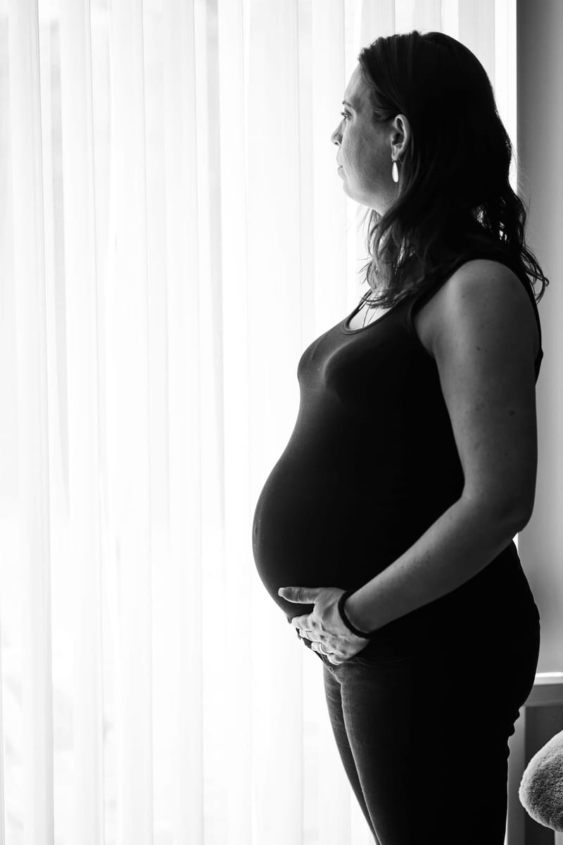 Zwangere vrouw in zwart-wit portret raakt buik aan, intieme maternity shoot thuis Zoetermeer — Familieshoot Stefan Segers